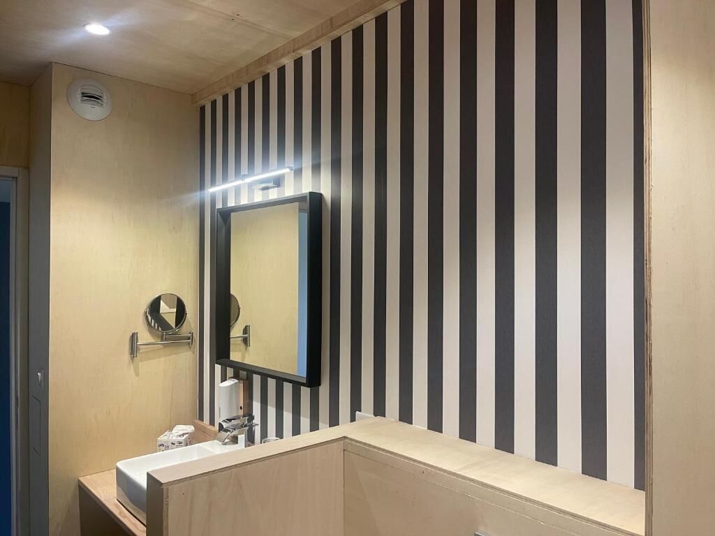 A bathroom with a striped wall, a mirror, and a sink.