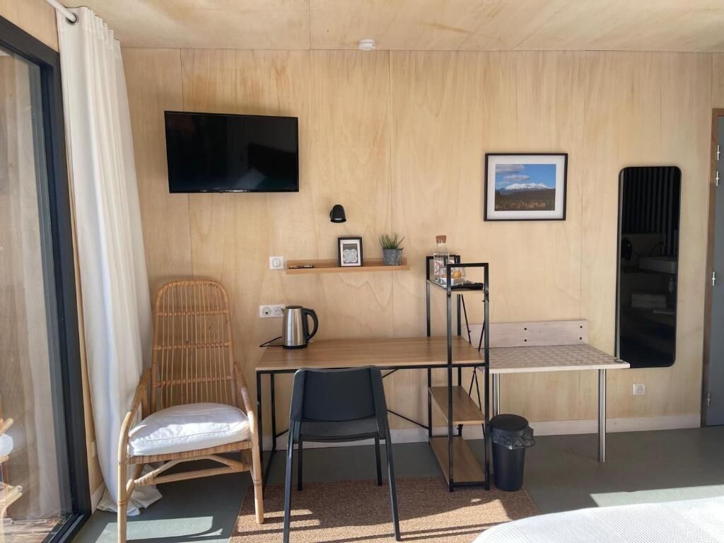 A room with a wooden desk, two chairs, a television, a framed picture, and a small shelf with items.