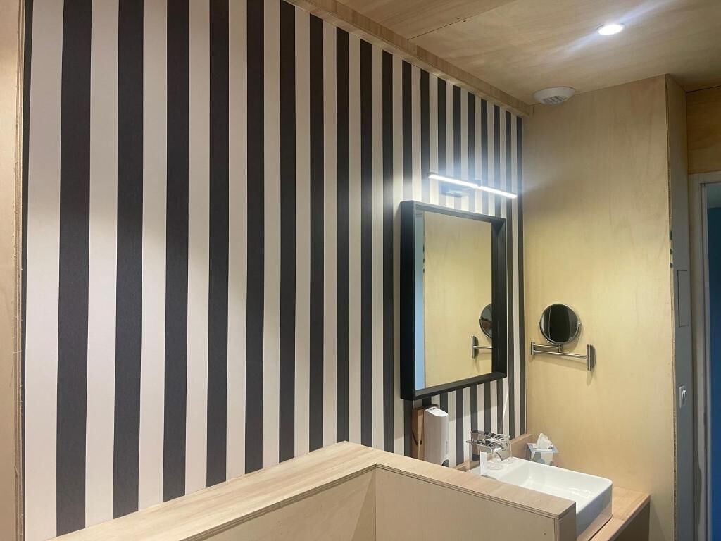 Un baño con pared a rayas, un espejo grande, un lavabo y un inodoro.