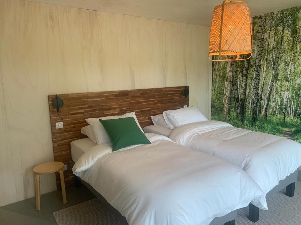 A bedroom with two beds, a wooden headboard, a small stool, and a hanging light fixture.