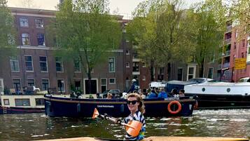 A person in a kayak on a canal with buildings and boats in the background.