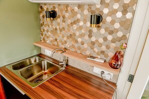 A compact kitchen with a double sink, a wooden countertop, a hexagonal patterned backsplash, and two wall-mounted light fixtures.