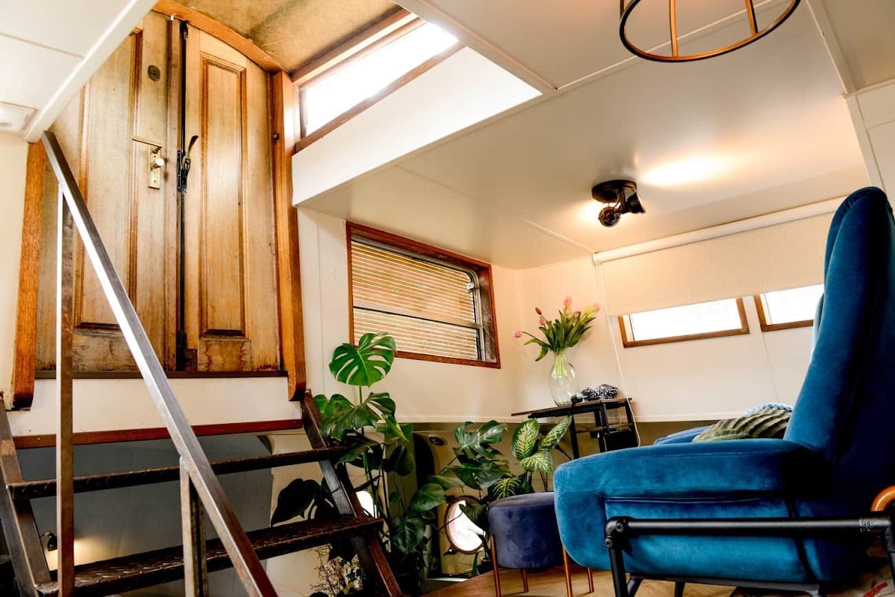 A room with a wooden staircase, a blue chair, and various plants.