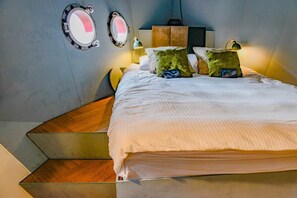 Een hotelkamer met een bed, twee bedlampen, een spiegel en een houten trap.