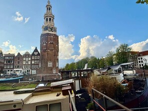 A historic tower with a clock, surrounded by traditional buildings and a modern structure with a boat.