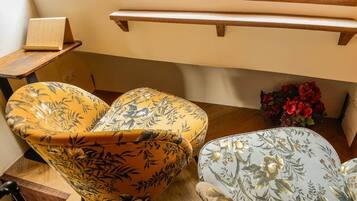 A corner of a room with two upholstered chairs with floral patterns, a small table with a book, and a vase with red flowers.
