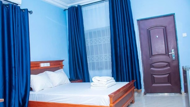 A bedroom with a wooden bed, blue curtains, a window with a geometric pattern, and a brown door.