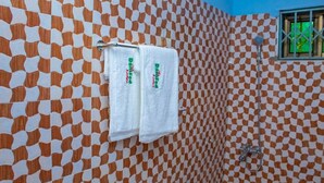 A bathroom with patterned tiles, a towel rack with two towels, a shower head, and a window with a view.