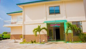 A building with a reception area, a balcony, and a small garden with palm trees.