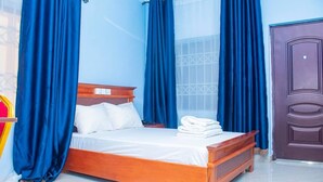 A bedroom with a wooden bed, blue curtains, a white bedside table, and a brown door.