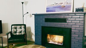 Un salon avec une cheminée, un tableau encadré, un fauteuil, une table et un lampadaire.