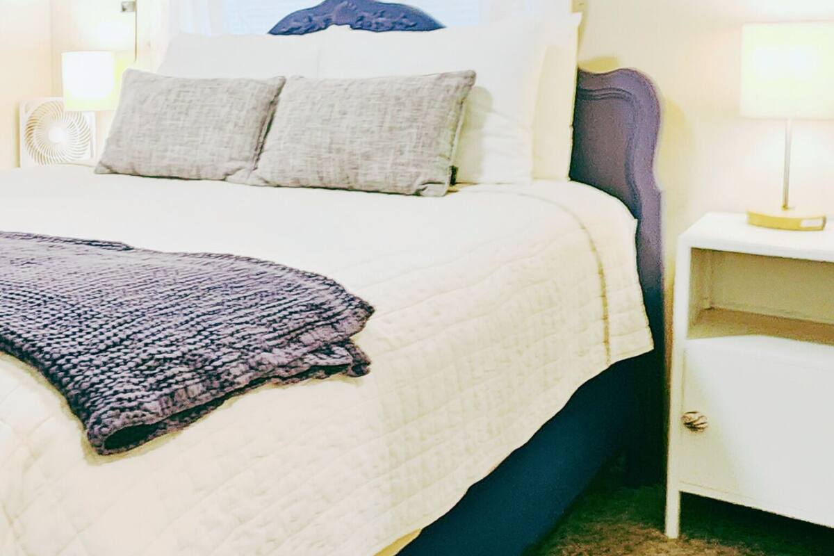 A neatly made bed with a white duvet, a blue headboard, and a bedside table with a lamp.