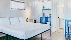 Une chambre avec un grand lit, un plancher en bois, un plafond à carreaux, une petite kitchenette et une salle de bain visible à travers une porte ouverte.