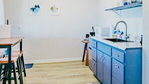 Une cuisine de taille réduite, dotée d’un plan de travail bleu, d’un évier et d’un coin repas avec une table et des chaises.