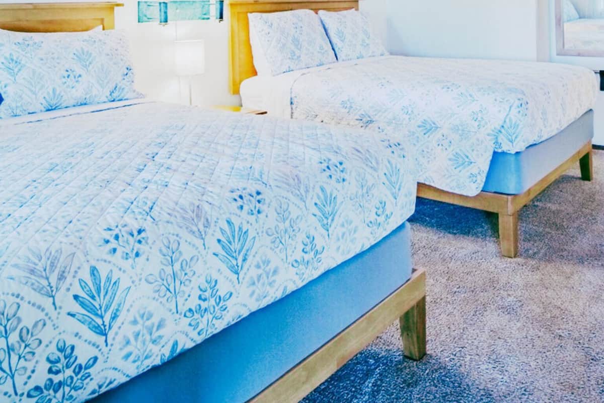 A room with two beds, a wooden ceiling, white walls, and a window.