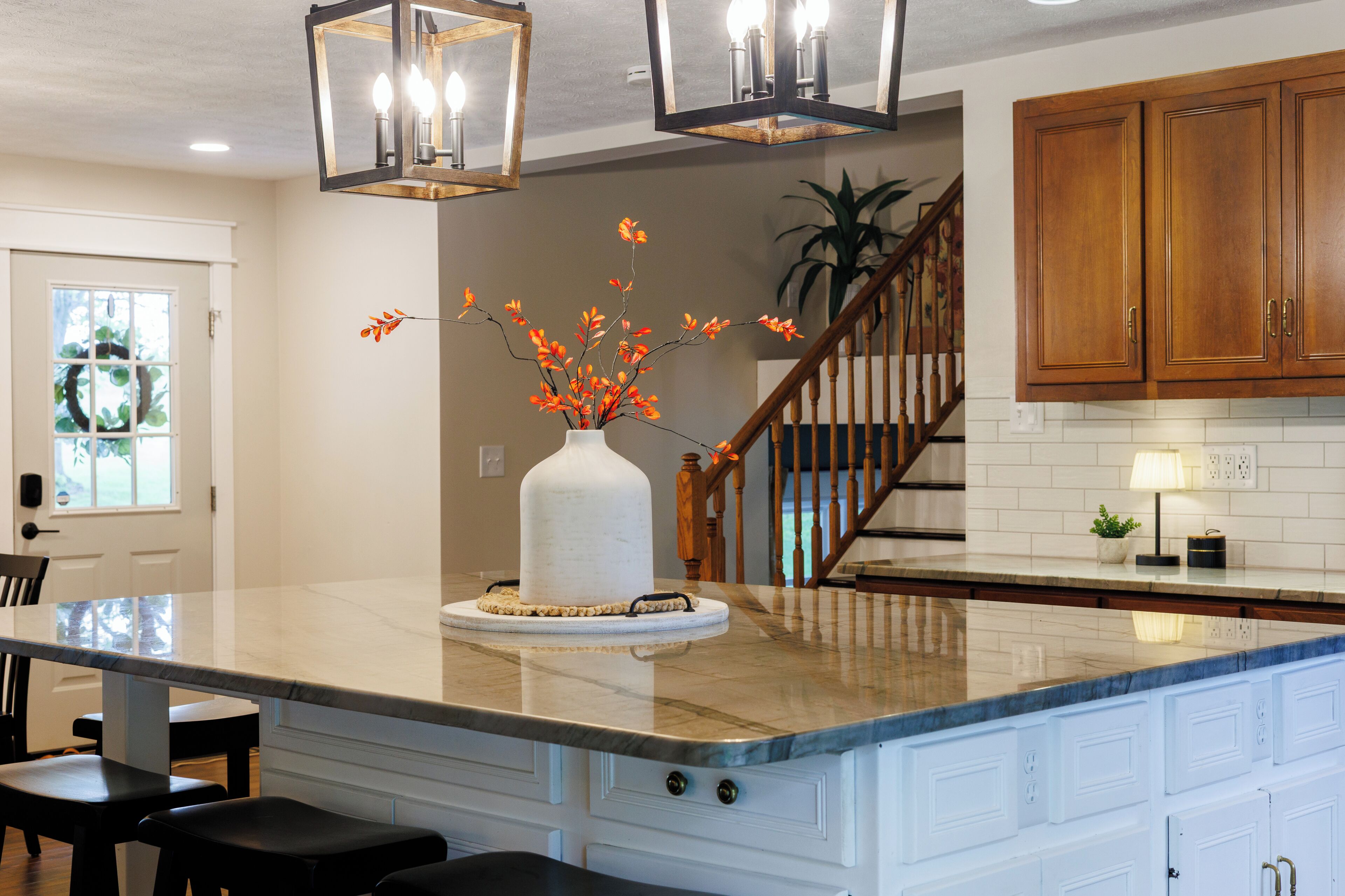 A kitchen with a marble island, wooden cabinets, and a vase with orange flowers.