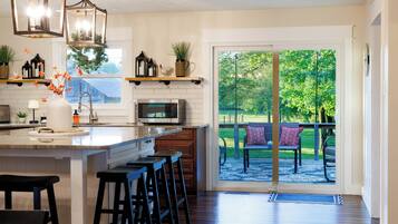 A kitchen with a large island, bar stools, a microwave, and a view of a patio with outdoor seating.