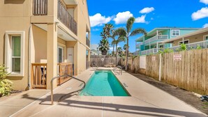 A residential building with a swimming pool, wooden fence, and palm trees. - Beachfront Condo with Private Balcony Pool (South Padre Island)