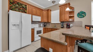 A kitchen with wooden cabinets, a white refrigerator, a stove, and a granite countertop. - Beachfront Condo with Private Balcony Pool (South Padre Island)