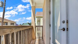 A balcony with a wooden railing, a sliding glass door, and a view of a neighboring building. - Beachfront Condo with Private Balcony Pool (South Padre Island)