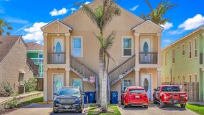 A two-story building with a central staircase, a parking area with two cars, and a small tree in front. - Beachfront Condo with Private Balcony Pool (South Padre Island)