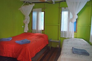 A room with two beds, one with a red bedspread and the other with a floral bedspread. There are white curtains on the windows, and a small table is visible in the corner. - Villa on the Caribbean Coast (Puerto Viejo de Talamanca)
