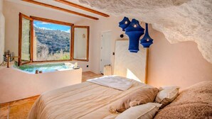 Un dormitorio con un ventanal grande, una bañera y una cama con almohadas.