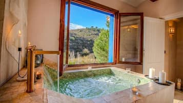 Un área de spa con jacuzzi, velas y vistas a una colina a través de una ventana.