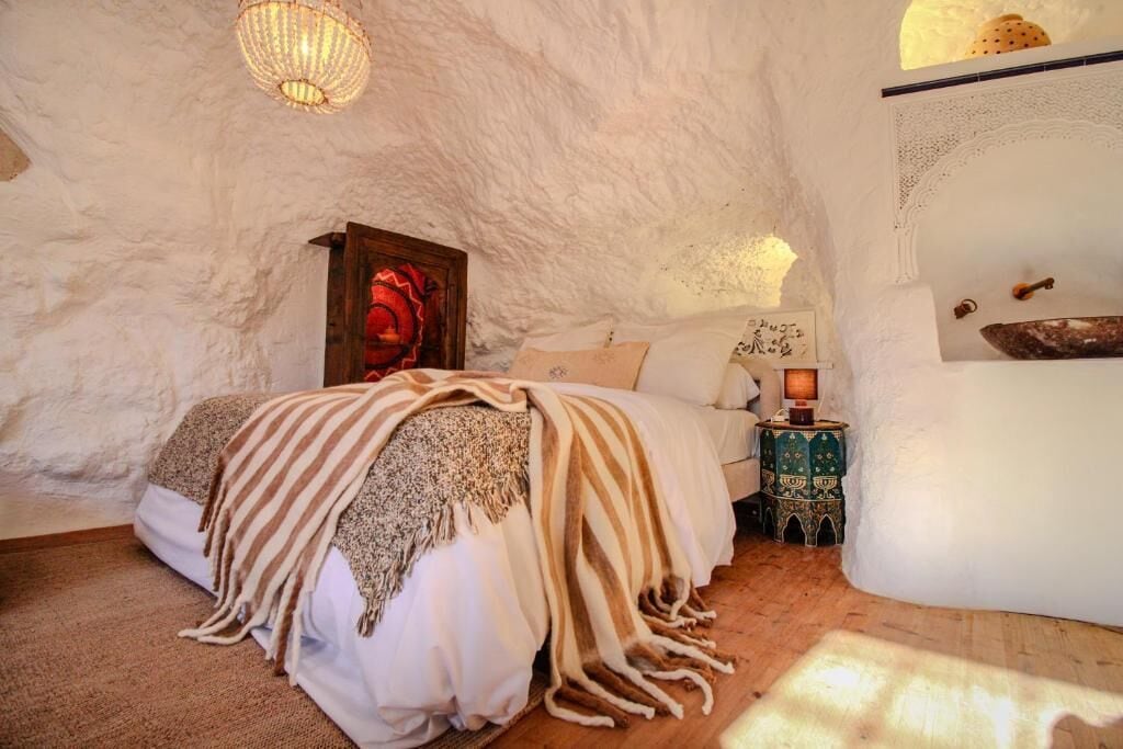 A cozy bedroom with a bed, a nightstand, a decorative lamp, and a wall-mounted shelf with a bowl.