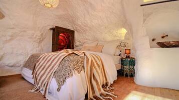 A cozy bedroom with a bed, a nightstand, a decorative lamp, and a wall-mounted shelf with a bowl.