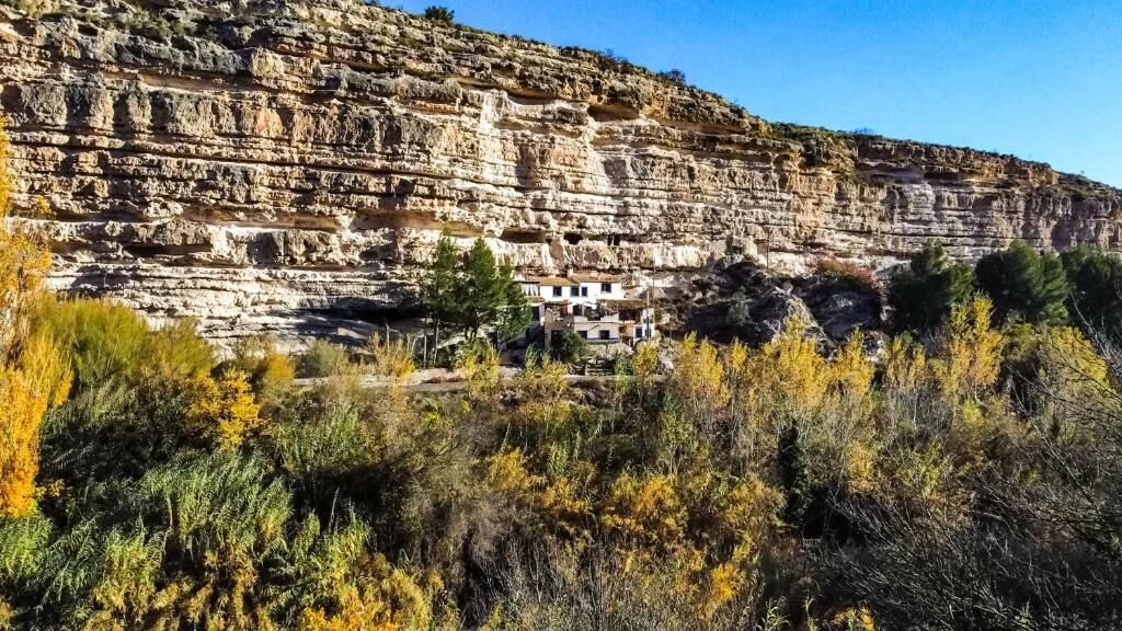 A cliffside with a building nestled at its base, surrounded by dense vegetation.