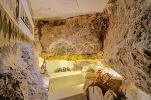 Una habitación con pared de roca natural, una bañera y un pequeño rincón de descanso con una planta.