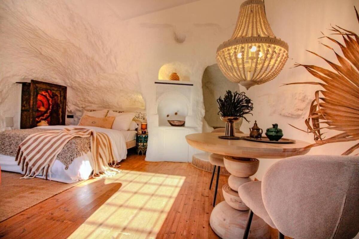 Un dormitorio acogedor con una cama, una mesa redonda de madera y una lámpara colgante.