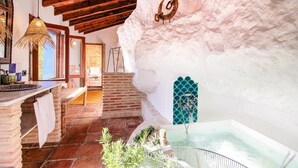 Un interior rústico con pared de piedra, techo de madera, zona de cocina y una bañera.