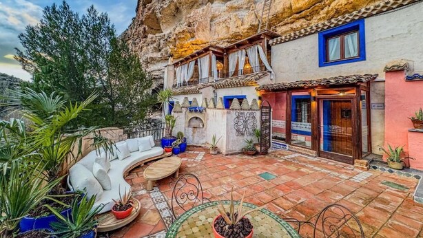 Un hotel con terraza, mobiliario exterior y vistas a un acantilado rocoso.