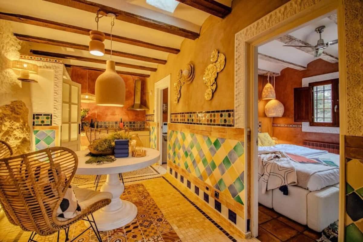 Una habitación con una mesa redonda, sillas de mimbre, una cama y un papel tapiz estampado.