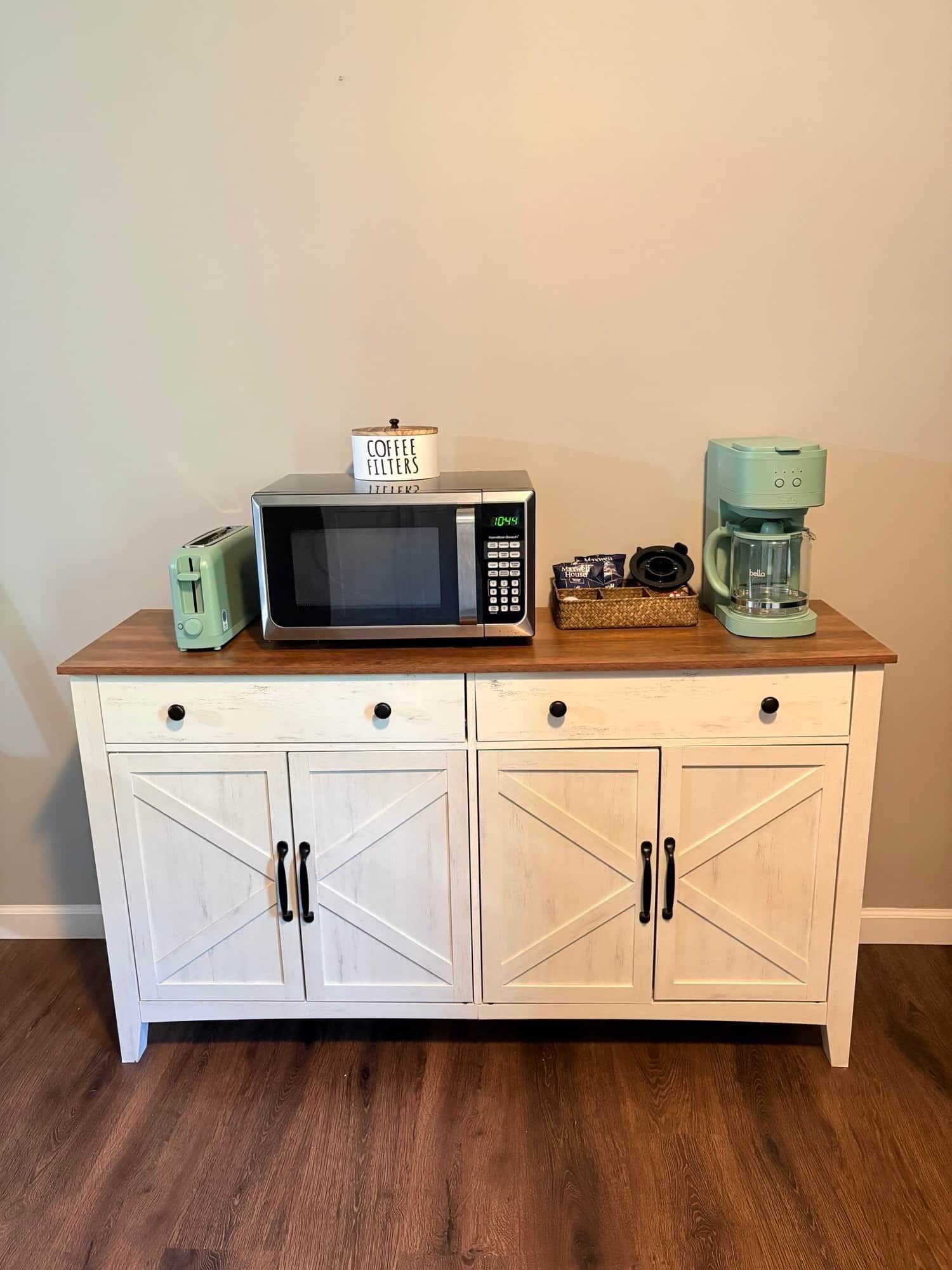 A kitchenette with a microwave, toaster, coffee maker, and a coffee filter container on a wooden countertop.