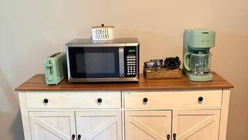A kitchenette with a microwave, toaster, coffee maker, and a coffee filter container on a wooden countertop.
