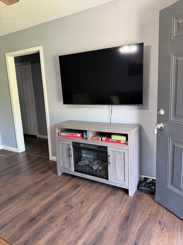 A room with a flat-screen TV mounted on the wall, a wooden entertainment center with game boxes, and a door with a key lock.