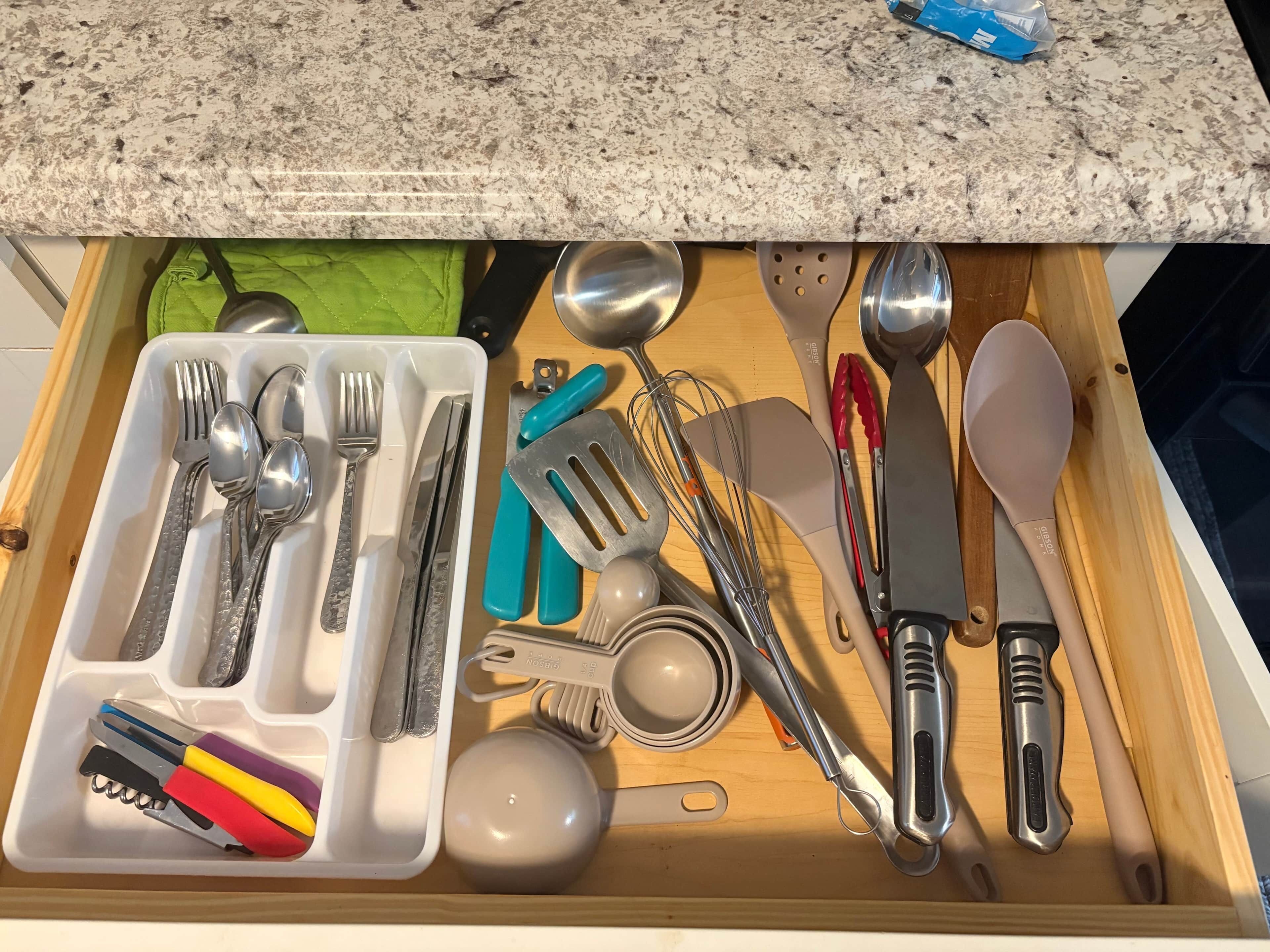 Eine Schublade mit Küchenutensilien, darunter Löffel, Gabeln, Messer und ein Multitool.