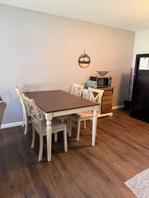 A dining area with a wooden table and chairs, a microwave, and a refrigerator.
