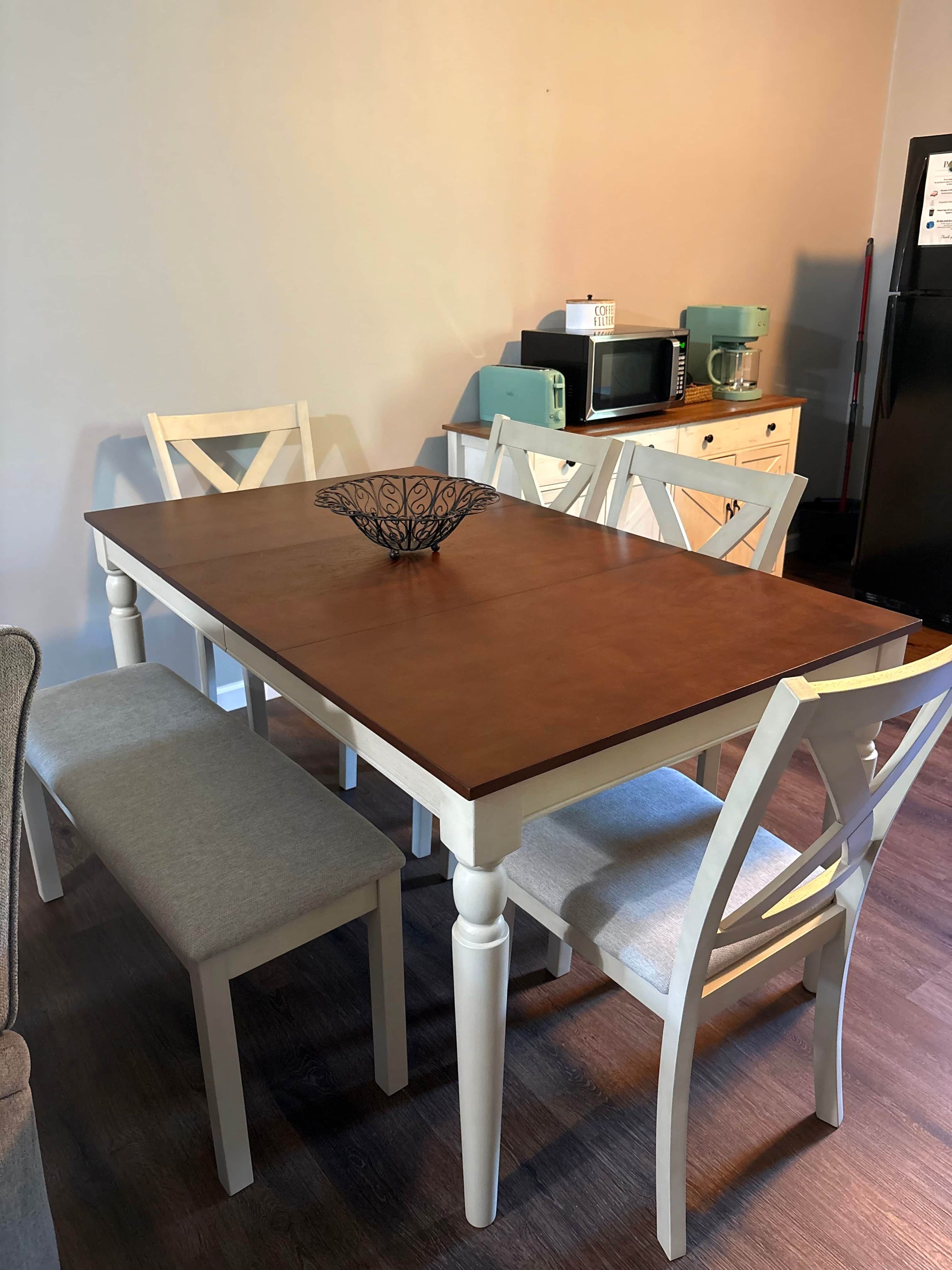 A dining table with a decorative bowl, surrounded by white chairs with cushioned seats.