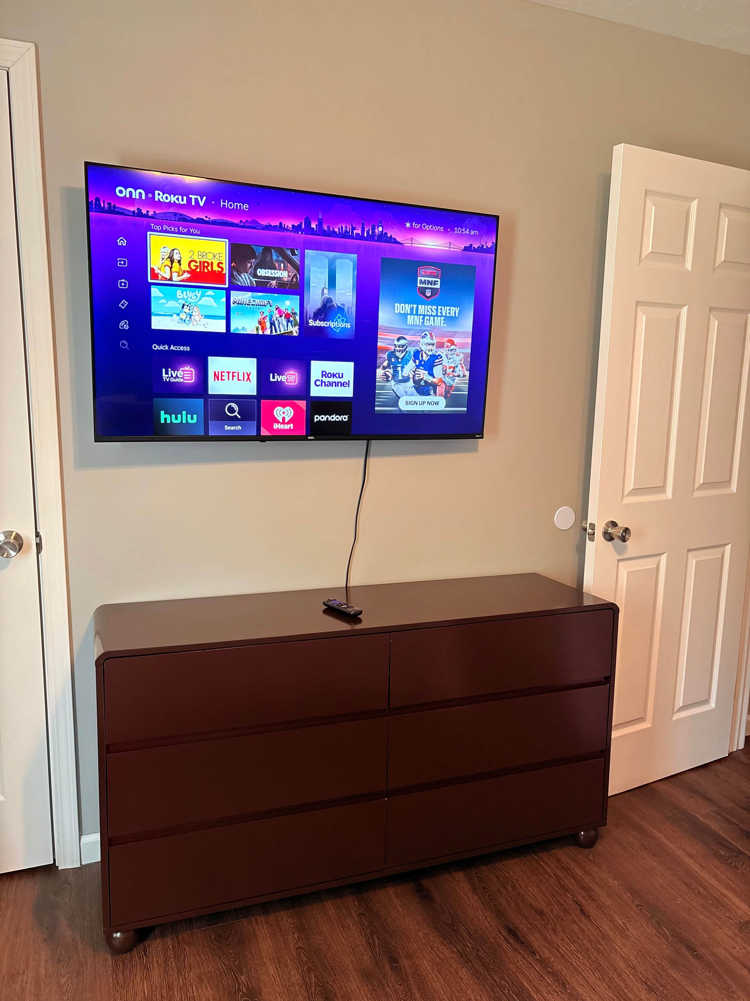 A flat-screen TV mounted on a wall with a dark wooden cabinet below it.
