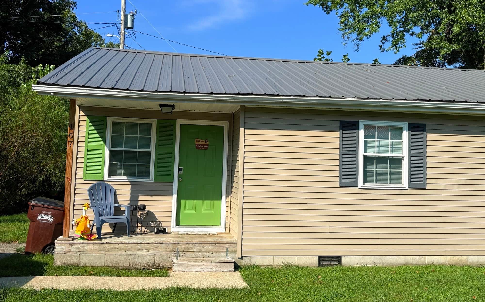 A single-story house with a green door, a small porch, and a trash bin labeled 'RUMPIRE'.