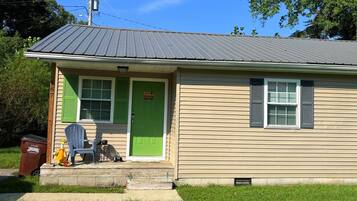 A single-story house with a green door, a small porch, and a trash bin labeled 'RUMPIRE'.