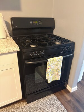A black stove with a digital clock, a microwave, and a patterned towel hanging on the oven door.