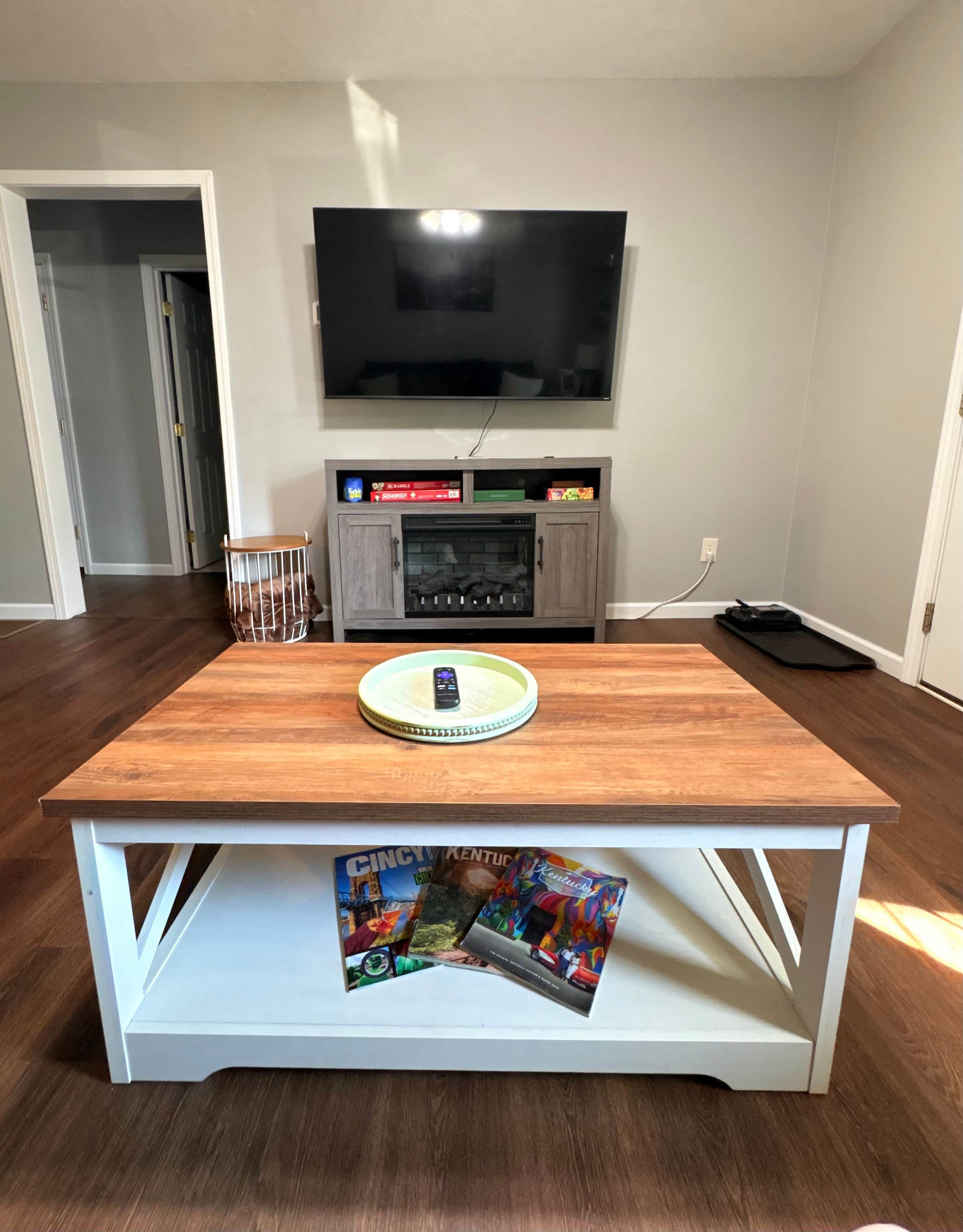 Un salon avec une table en bois, un téléviseur à écran plat fixé au mur et un meuble placé sous le téléviseur.