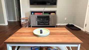 Un salon avec une table en bois, un téléviseur à écran plat fixé au mur et un meuble placé sous le téléviseur.
