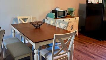 A dining area with a wooden table and white chairs, a coffee maker, and a refrigerator with a WiFi symbol.