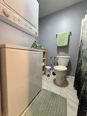 A compact bathroom with a washing machine, toilet, and a green rug.